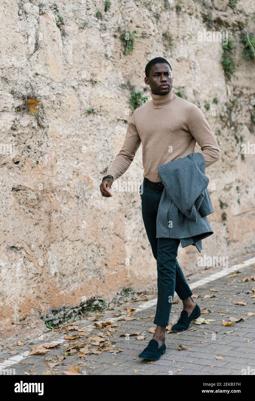 Young man holding jacket while walking on footpath Stock Photo