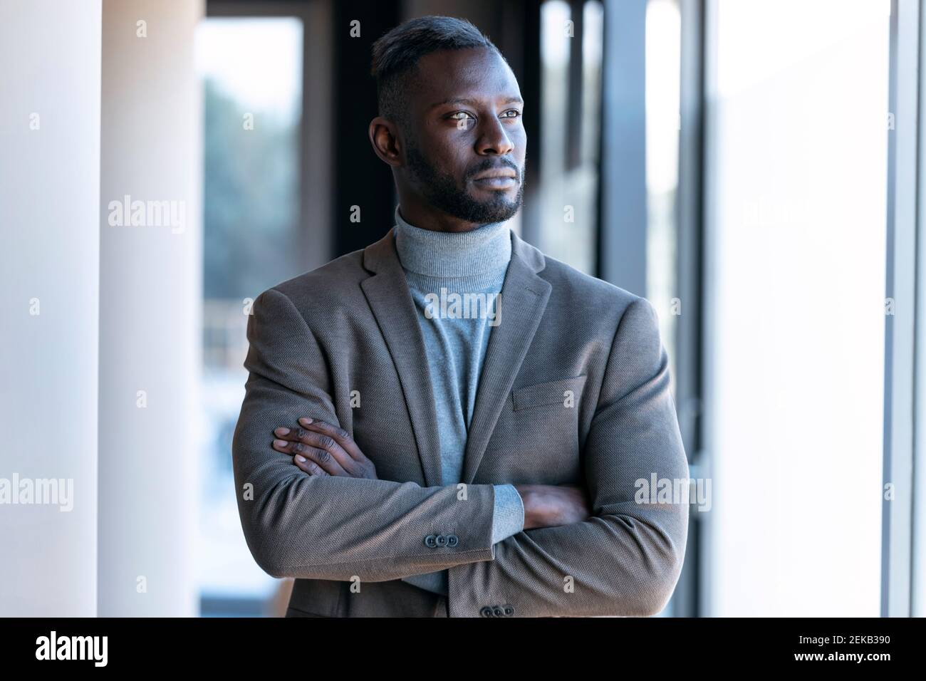 Thoughtful businessman looking away while standing with arms crossed in ...
