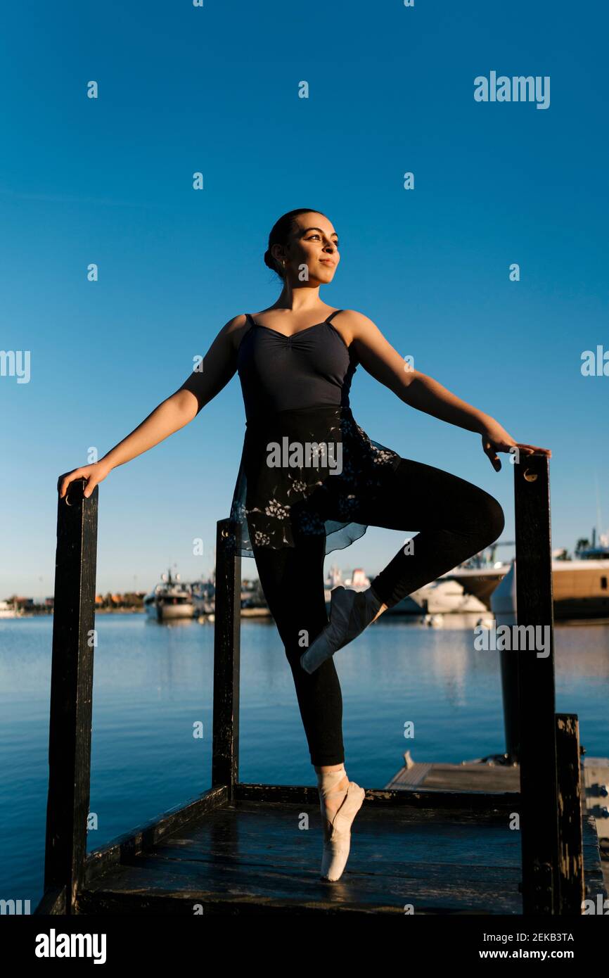 Female ballet dancer standing tiptoe while practicing on jetty against sky Stock Photo