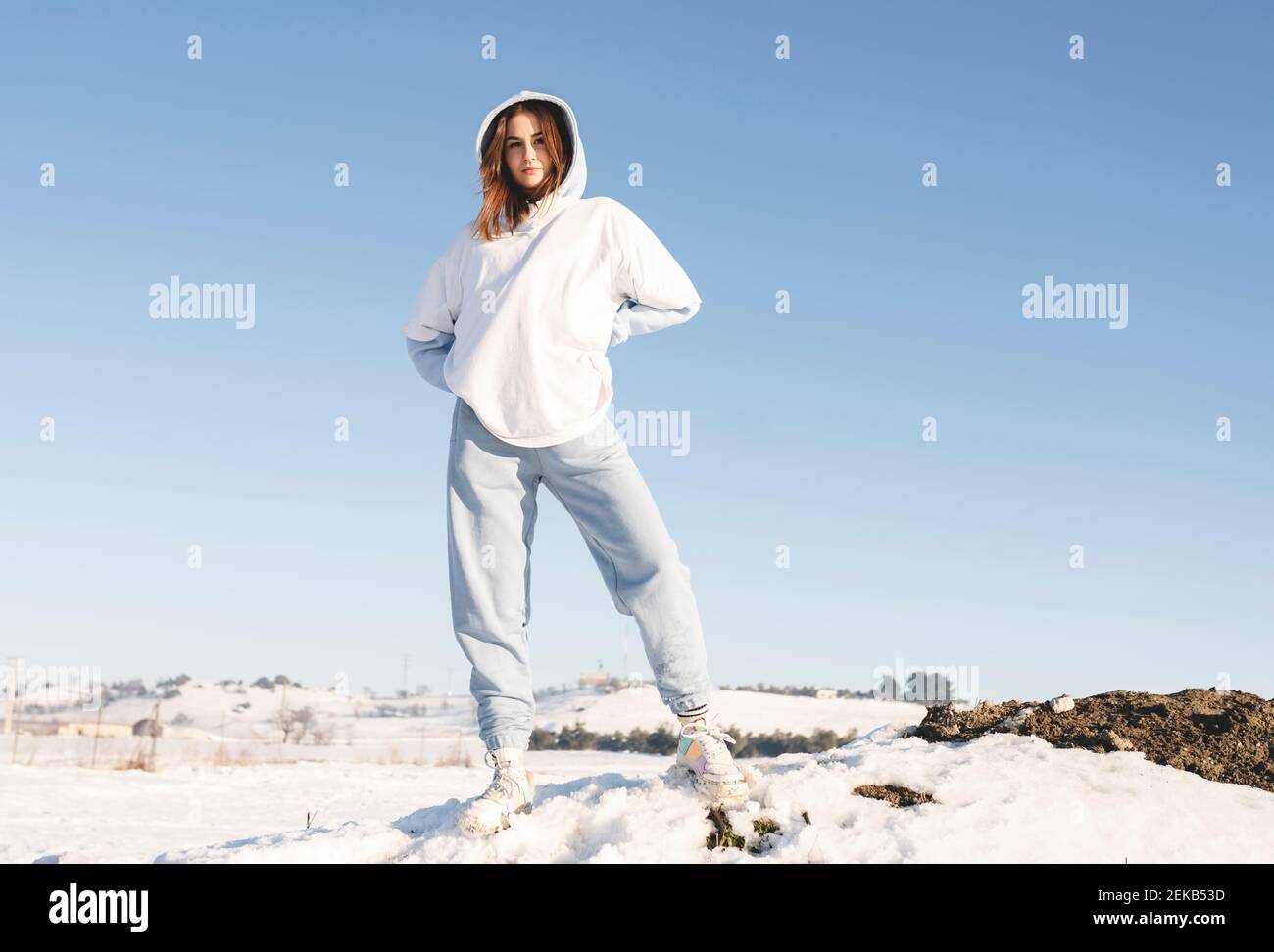 Woman wearing hood clothing standing with hand on hip against sky Stock Photo