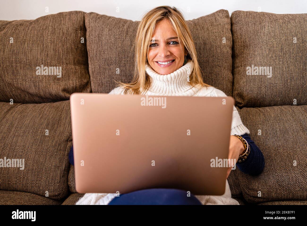 Smiling female therapist sitting with laptop on sofa at work place Stock Photo