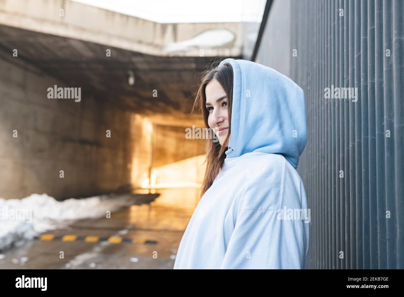 Smiling woman looking away while standing by wall Stock Photo