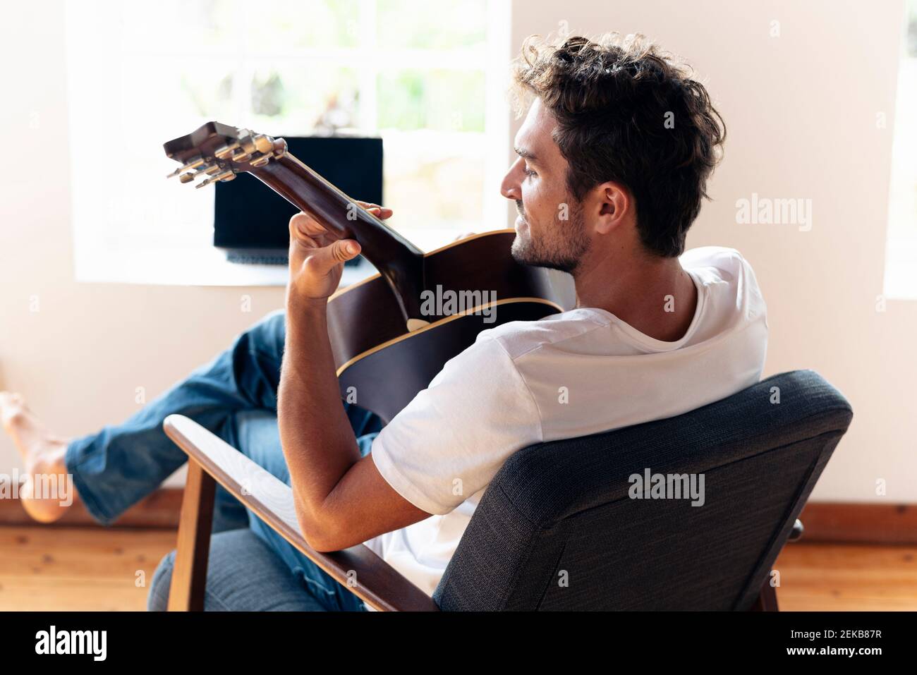 Smiling man playing guitar while relaxing on armchair at home Stock Photo