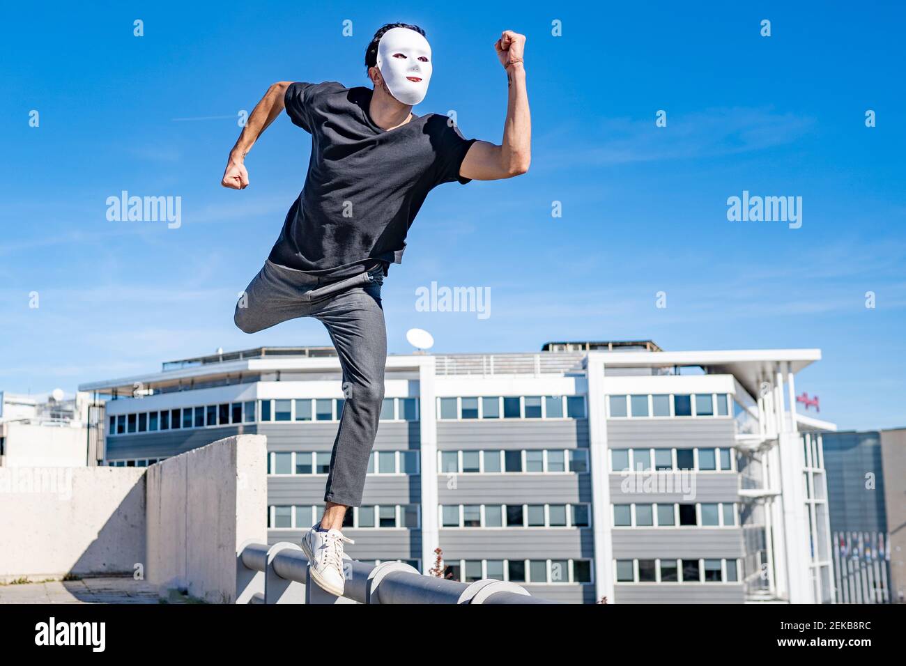 Young man wearing white mask running on rooftop during sunny day Stock Photo