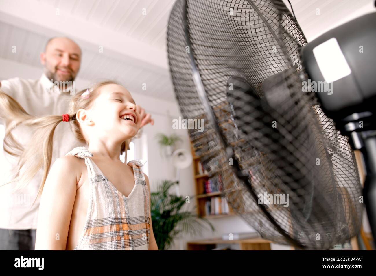 Girl in front of electric fan while father standing at home Stock Photo