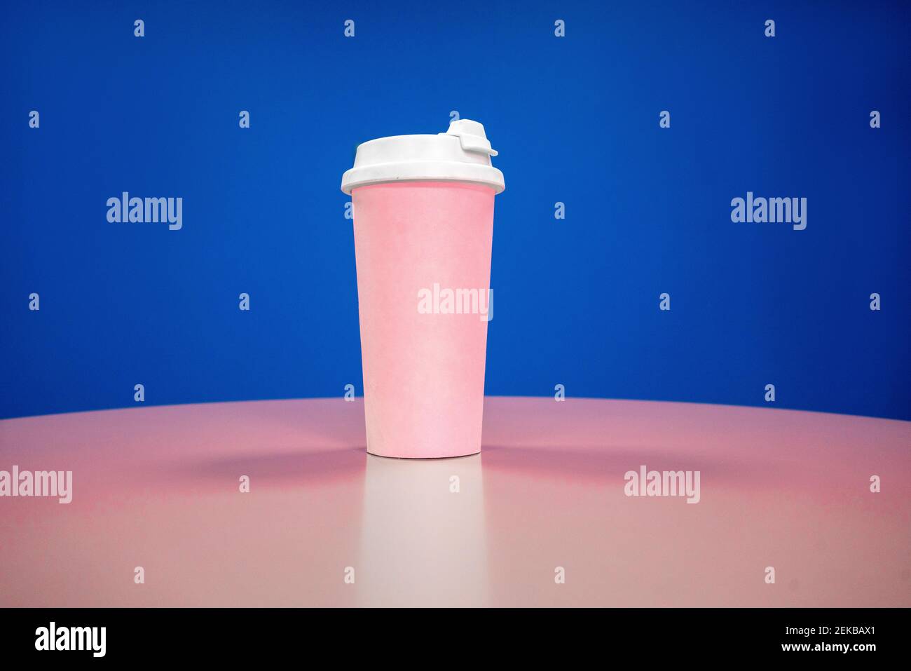 Pink reusable coffee cup on table against blue background Stock Photo