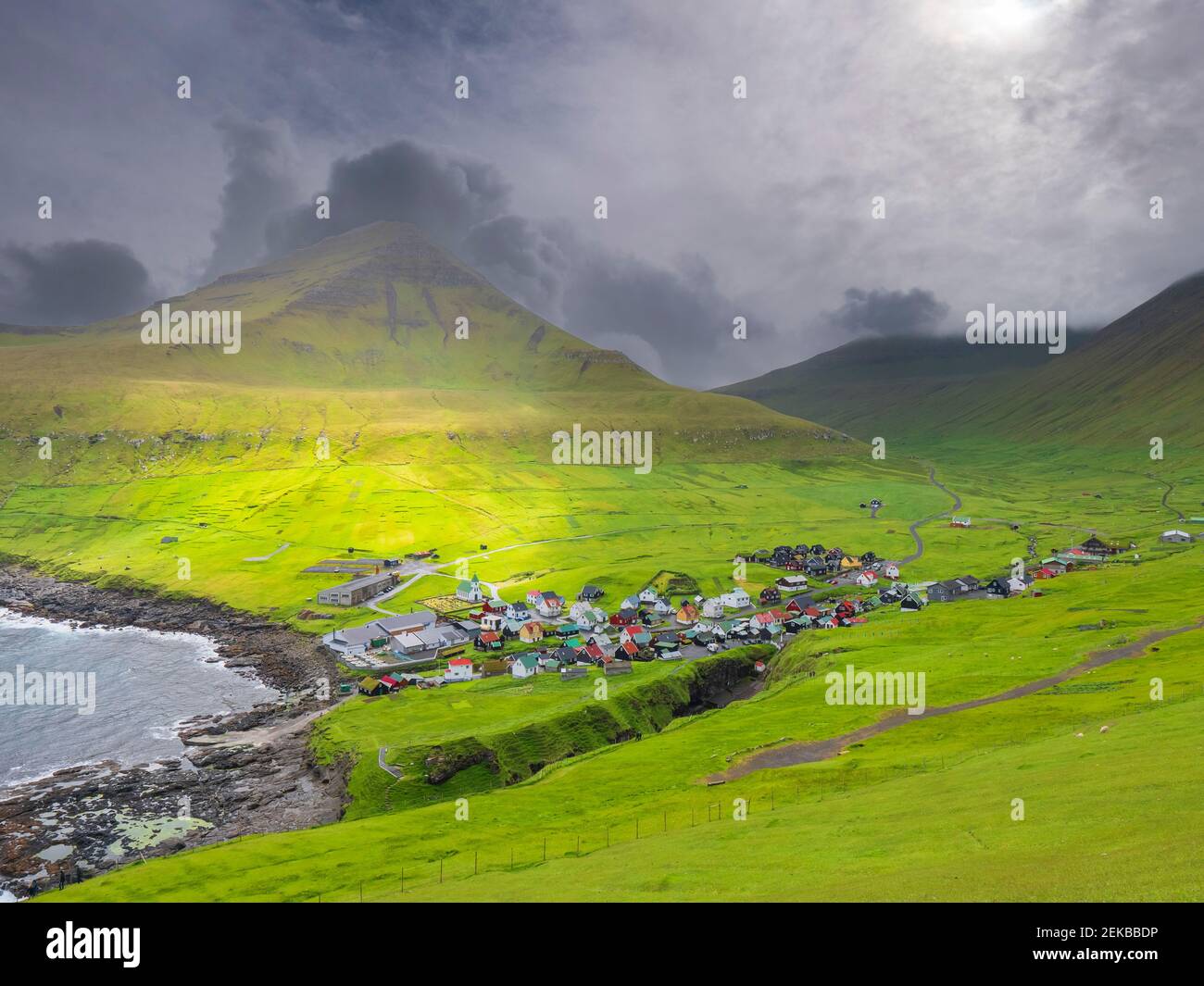 Green landscape and village by sea against cloudy sky, Iceland Stock Photo