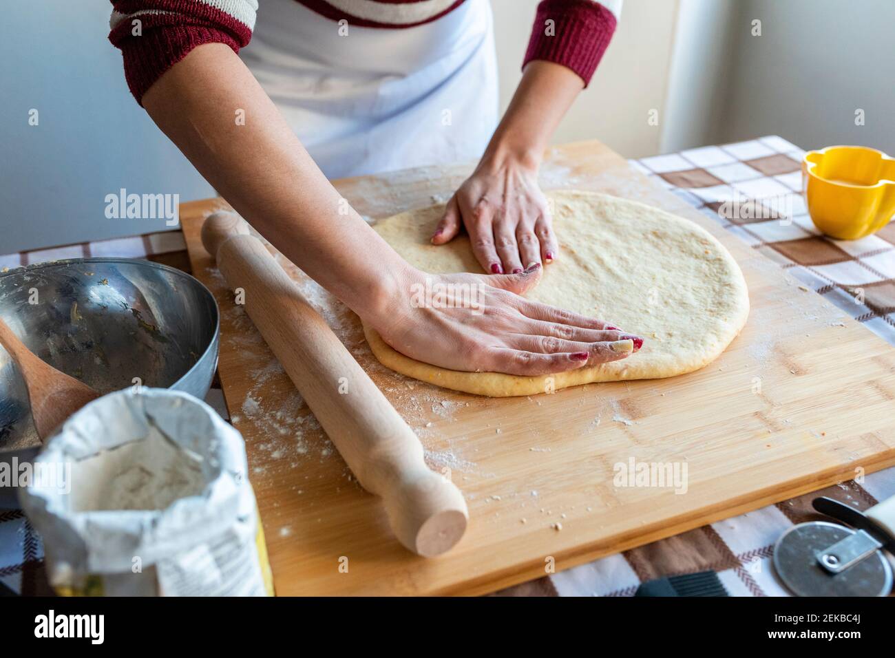 Woman flattening dough on cutting board with hands to make croissants in kitchen Stock Photo