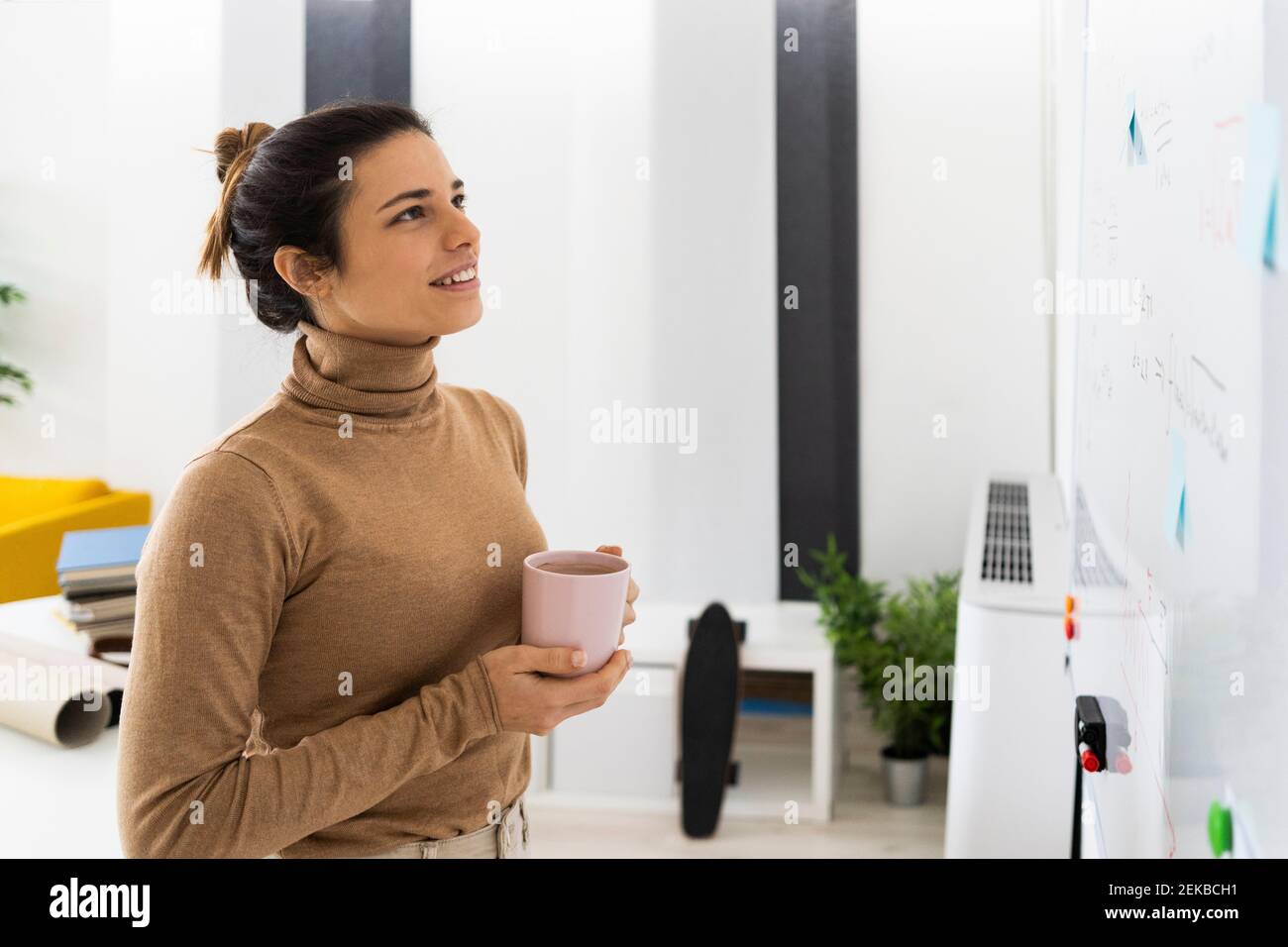 Woman with coffee cup looking at mathematical formula on board Stock Photo