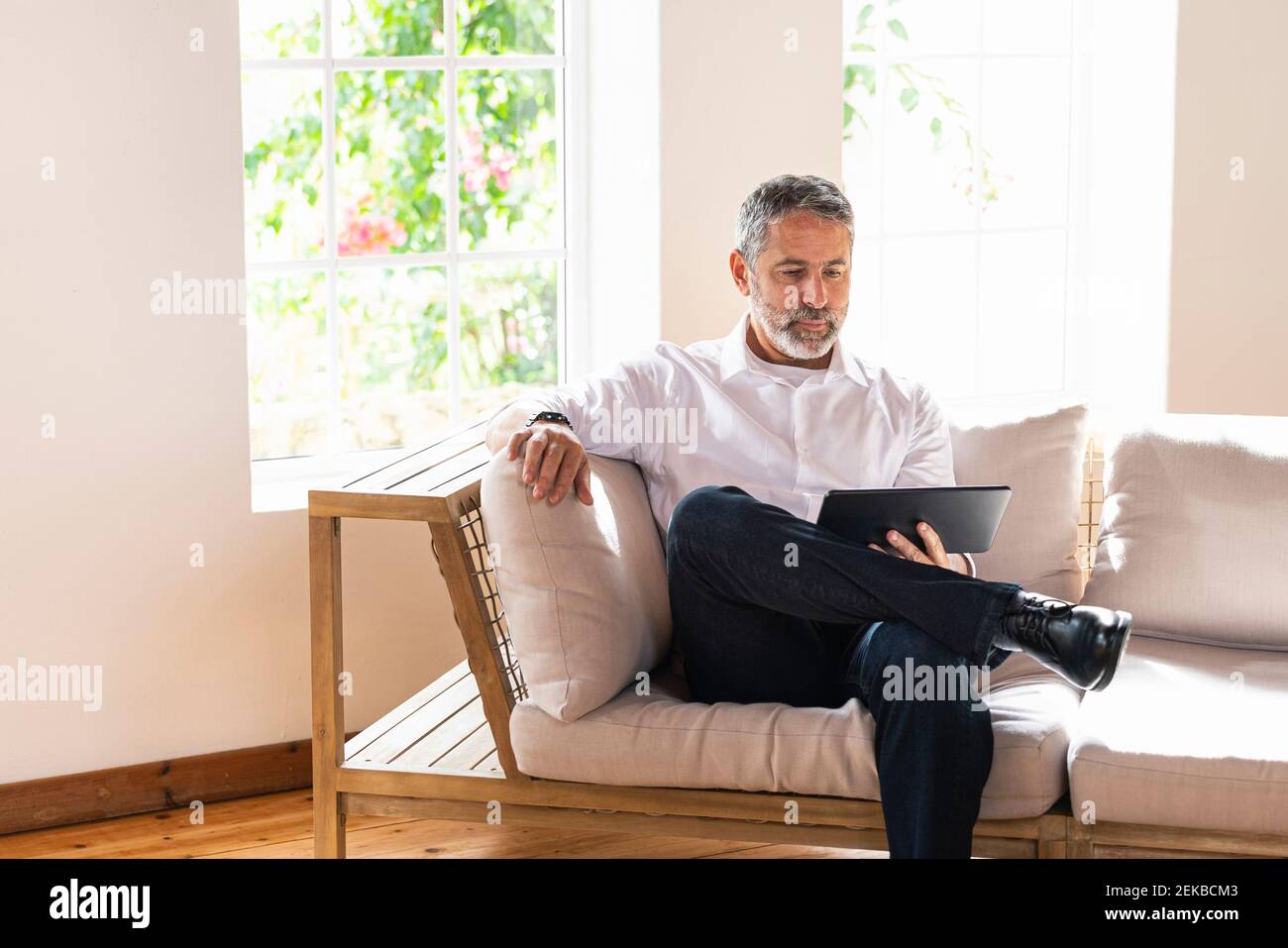 Mature businessman using digital tablet while sitting with legs crossed at knee on sofa at home Stock Photo