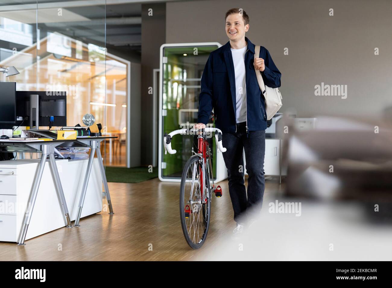 Smiling businessman with bag and bicycle walking while leaving after work from office Stock Photo