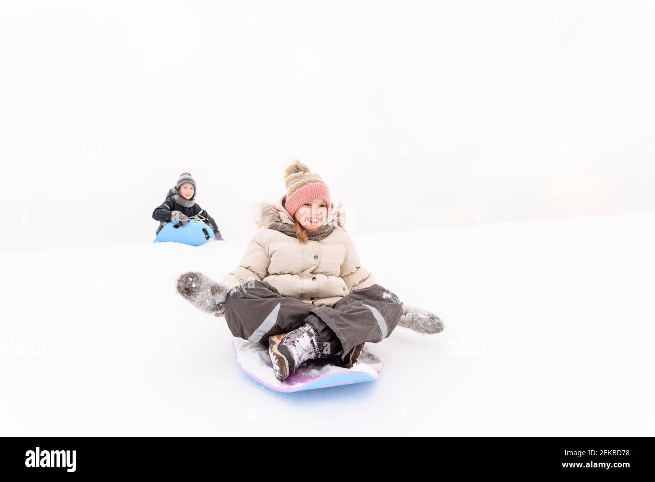 Playful siblings sledding on snow covered hill Stock Photo