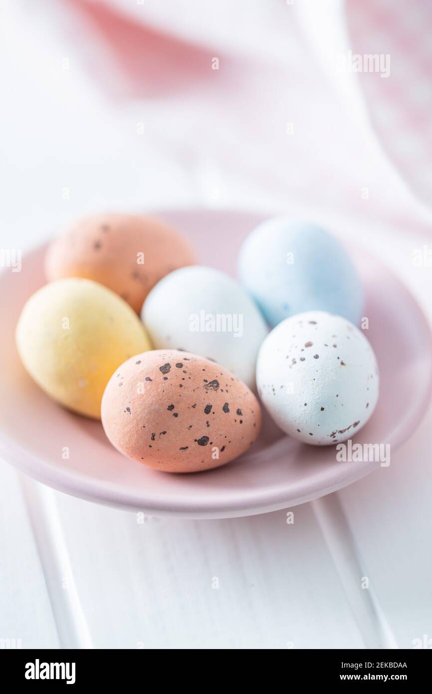 Chocolate easter eggs. Sweet candy eggs on pink plate on white table. Stock Photo