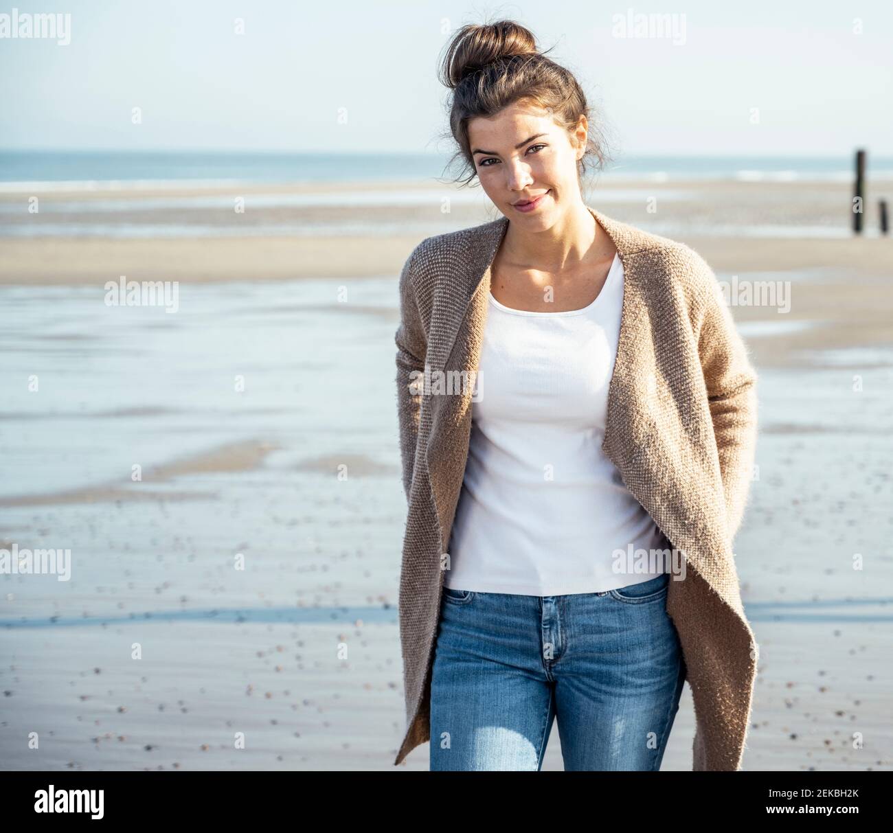 Beautiful woman with hands in pockets walking on beach during sunny day ...