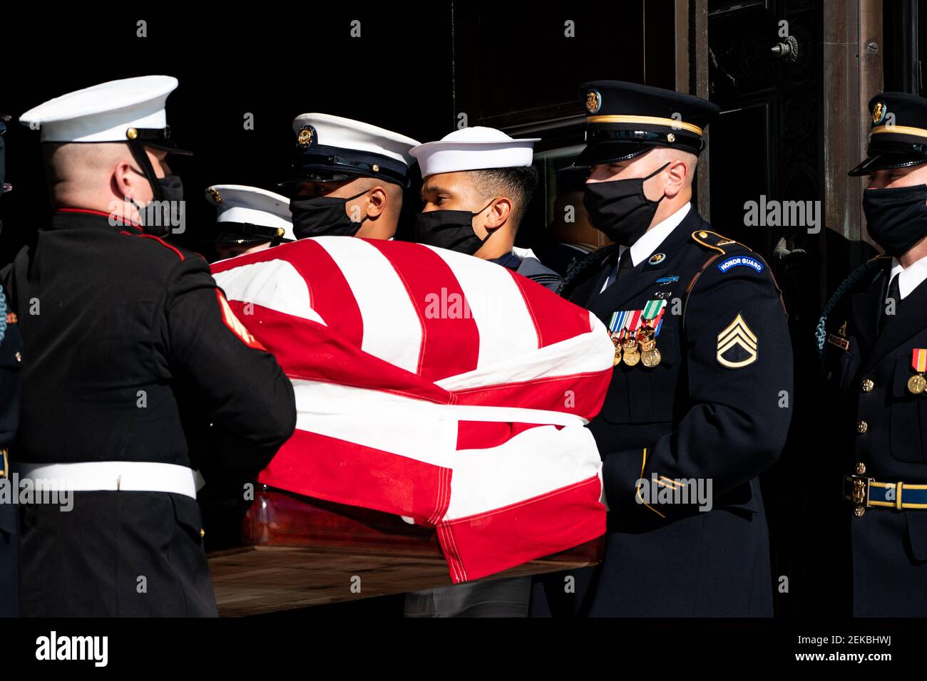Members of the Military, wearing face masks, carry flag draped casket