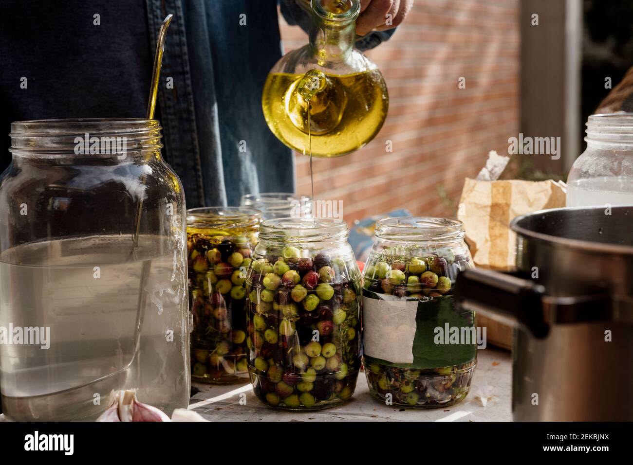 Senior man pouring olive oil in glass jar on table Stock Photo