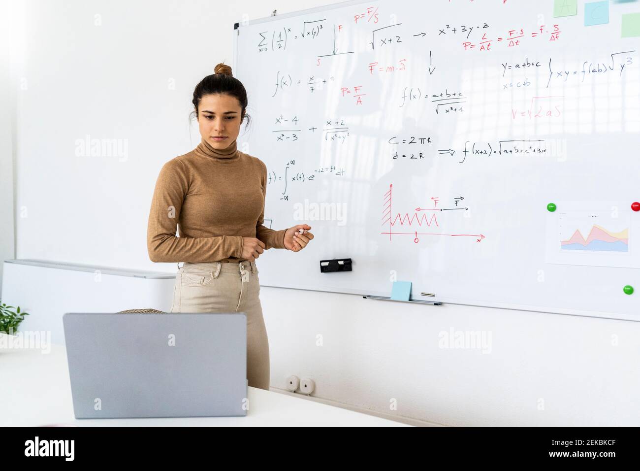 Woman looking at laptop while solving mathematical formula in living room Stock Photo