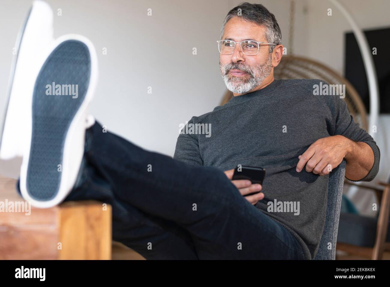 Thoughtful businessman using mobile phone while sitting with legs on table at home Stock Photo