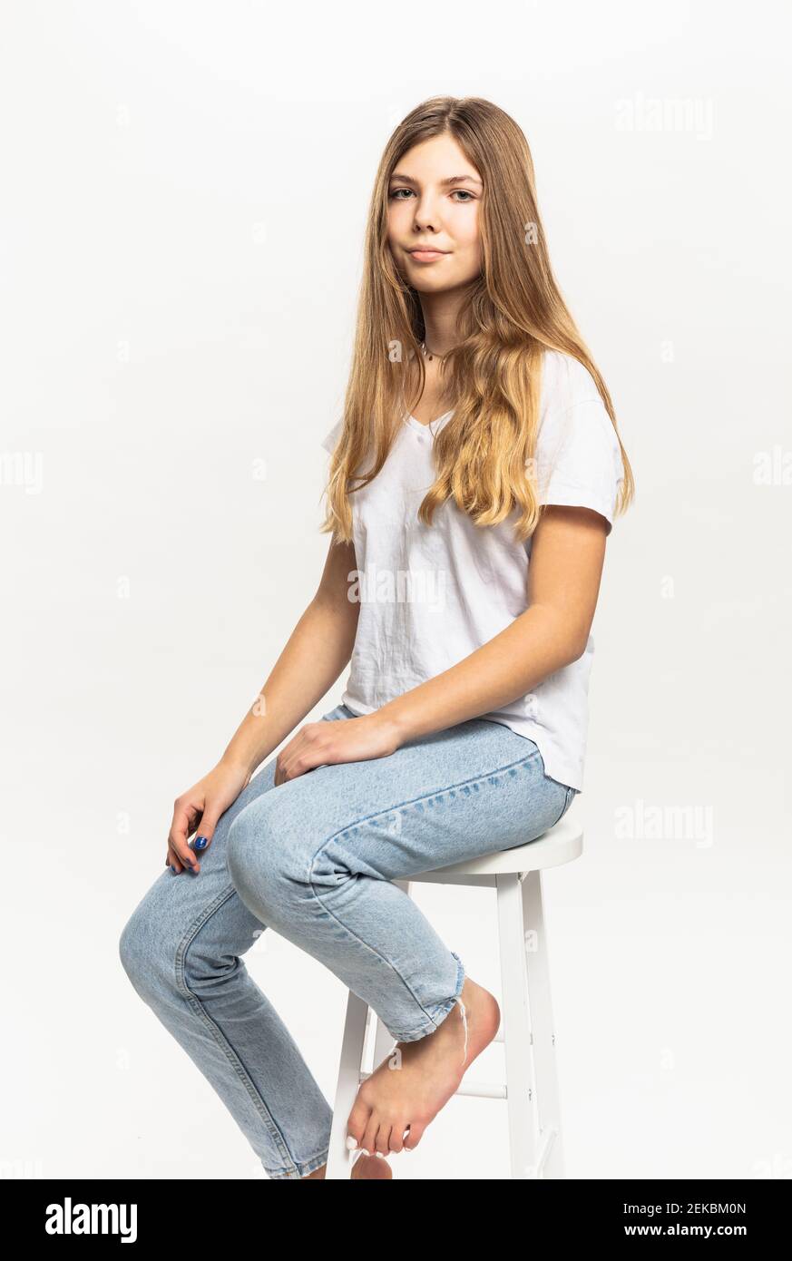 Pre-adolescent girl sitting on stool against white background in studio Stock Photo