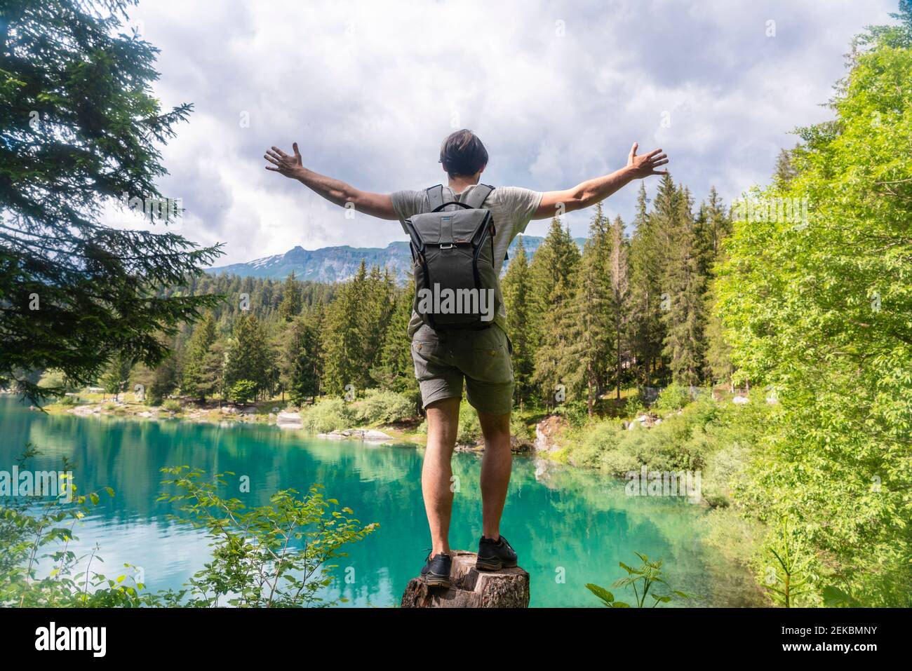 Carefree man carrying backpack standing with arms outstretched against Cauma Lake at Graubunden Canton, Switzerland Stock Photo