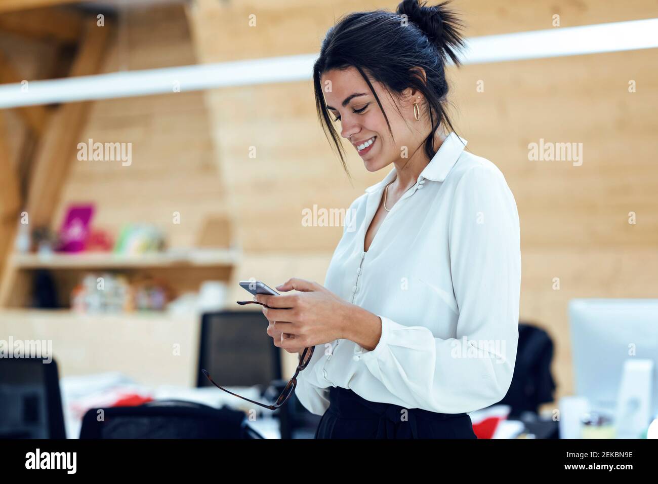 Texting Through Phone Smiling female entrepreneur texting through mobile phone at office ...