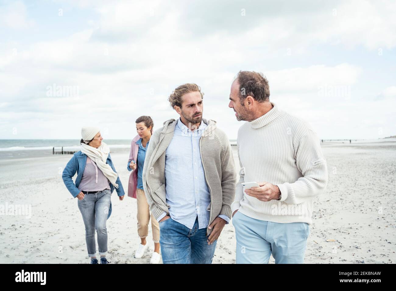 Two men walking and talking side by side along sandy beach Stock Photo