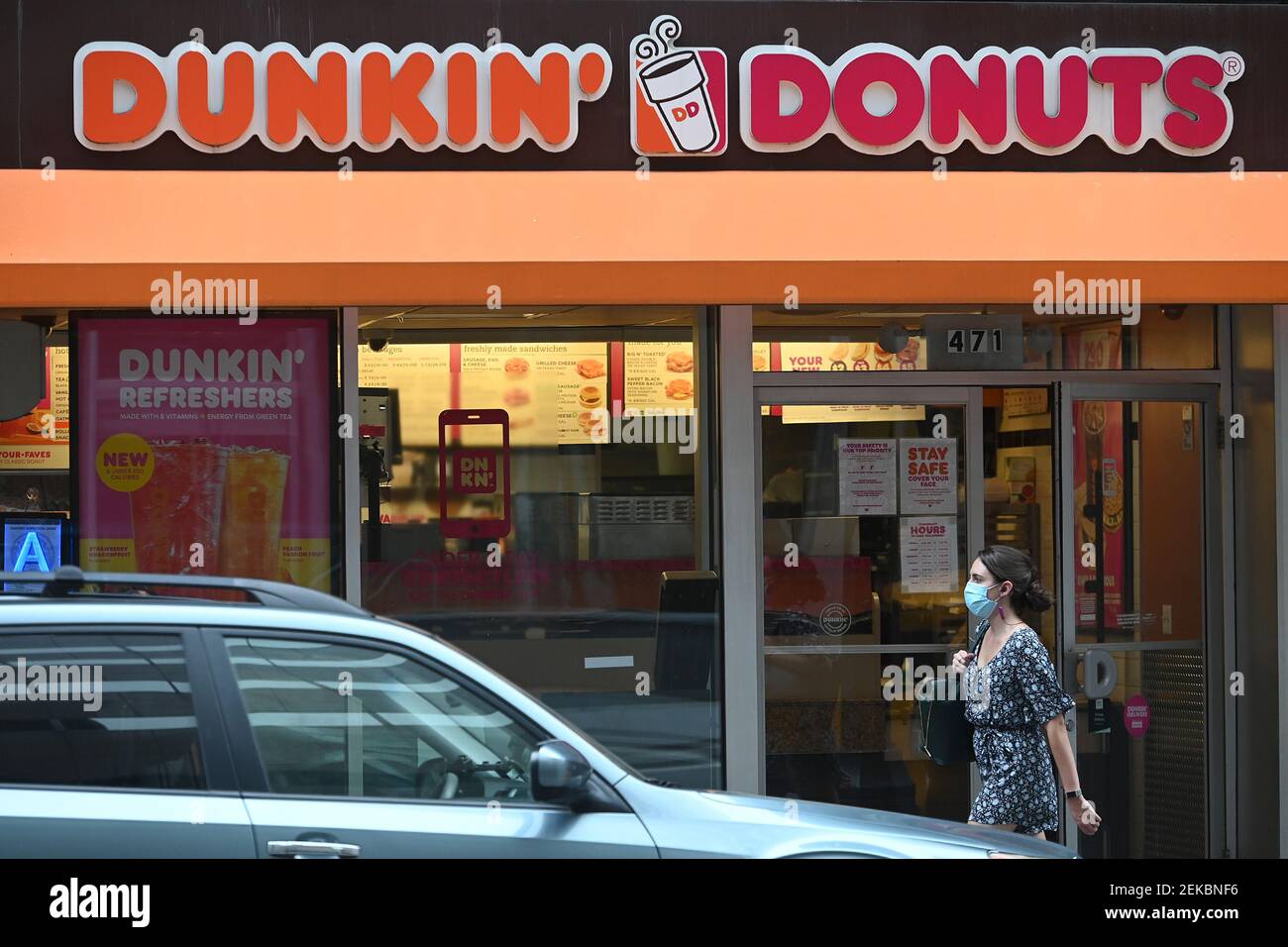 A woman wearing a mask walks past a Dunkin’ Donuts in Manhattan, as the
