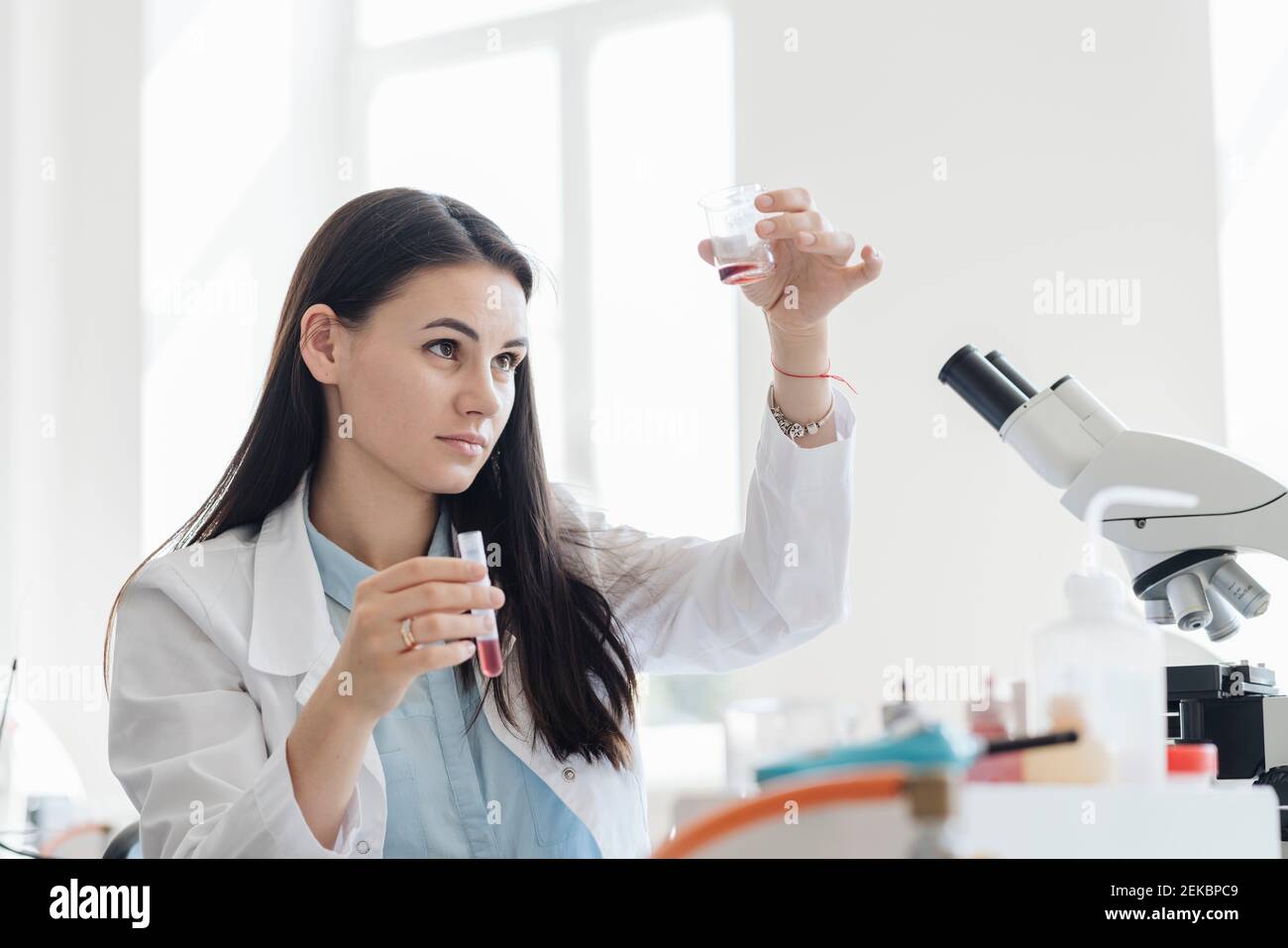 Young female researcher in white coat analyzing laboratory sample Stock Photo