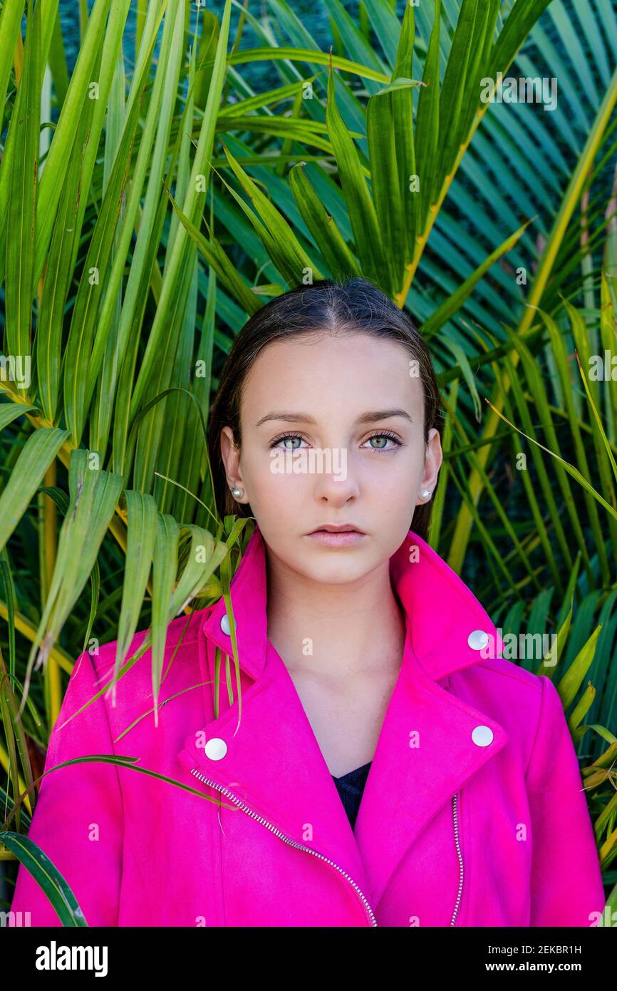 Close-up of serious teenage girl wearing pink coat against plants in yard Stock Photo
