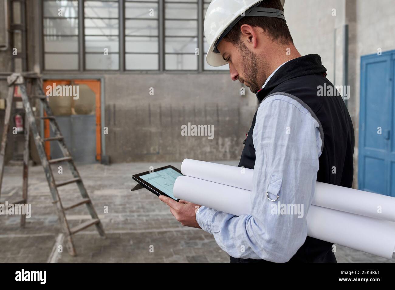 Male architect with blueprints using digital tablet while standing in building Stock Photo