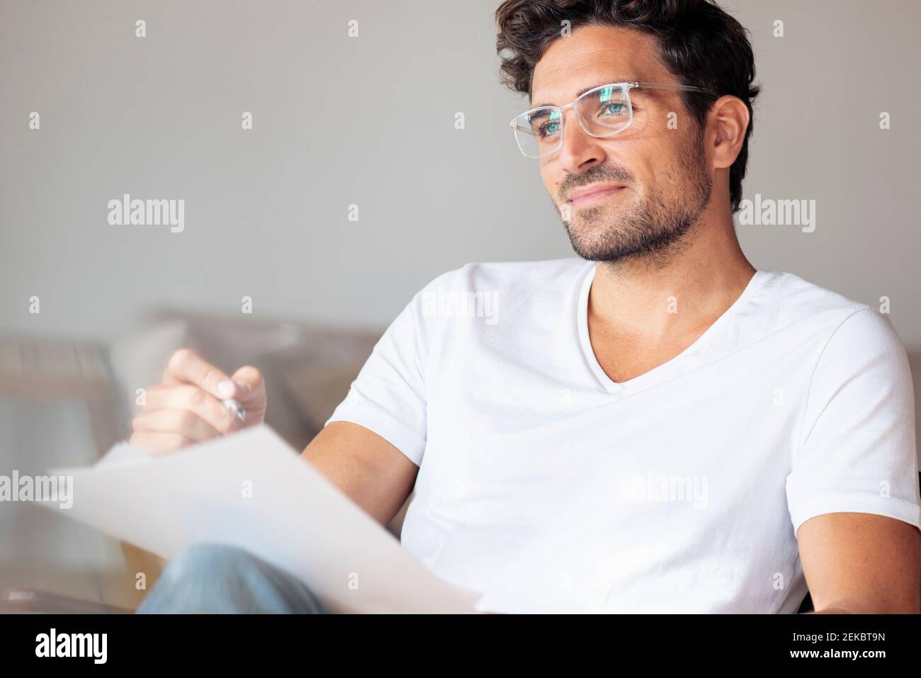 Thoughtful man with paper looking away while sitting at home Stock Photo