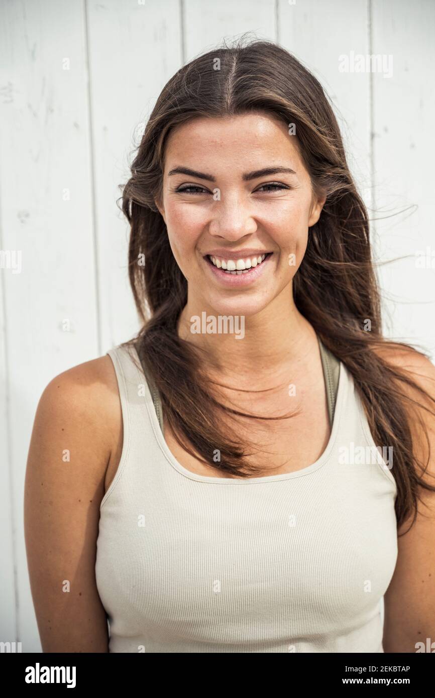 Happy young woman in tank top against beach hut Stock Photo
