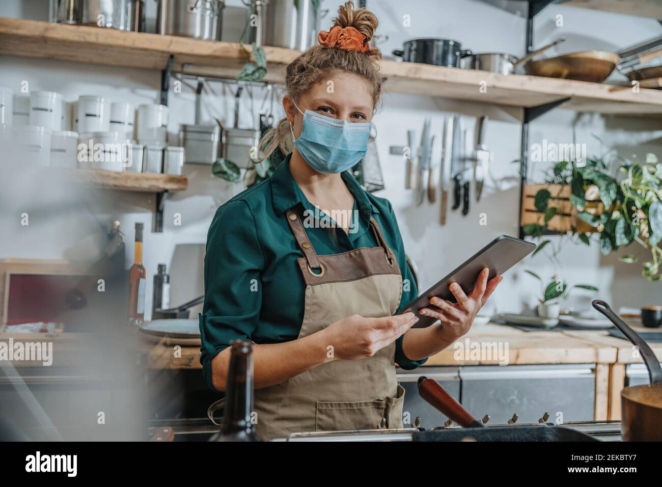 Female chef wearing protective face mask using digital tablet while standing in kitchen Stock Photo