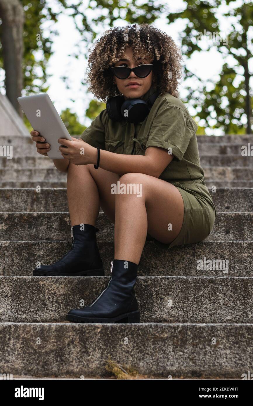 Woman holding digital tablet sitting on staircase against trees Stock Photo