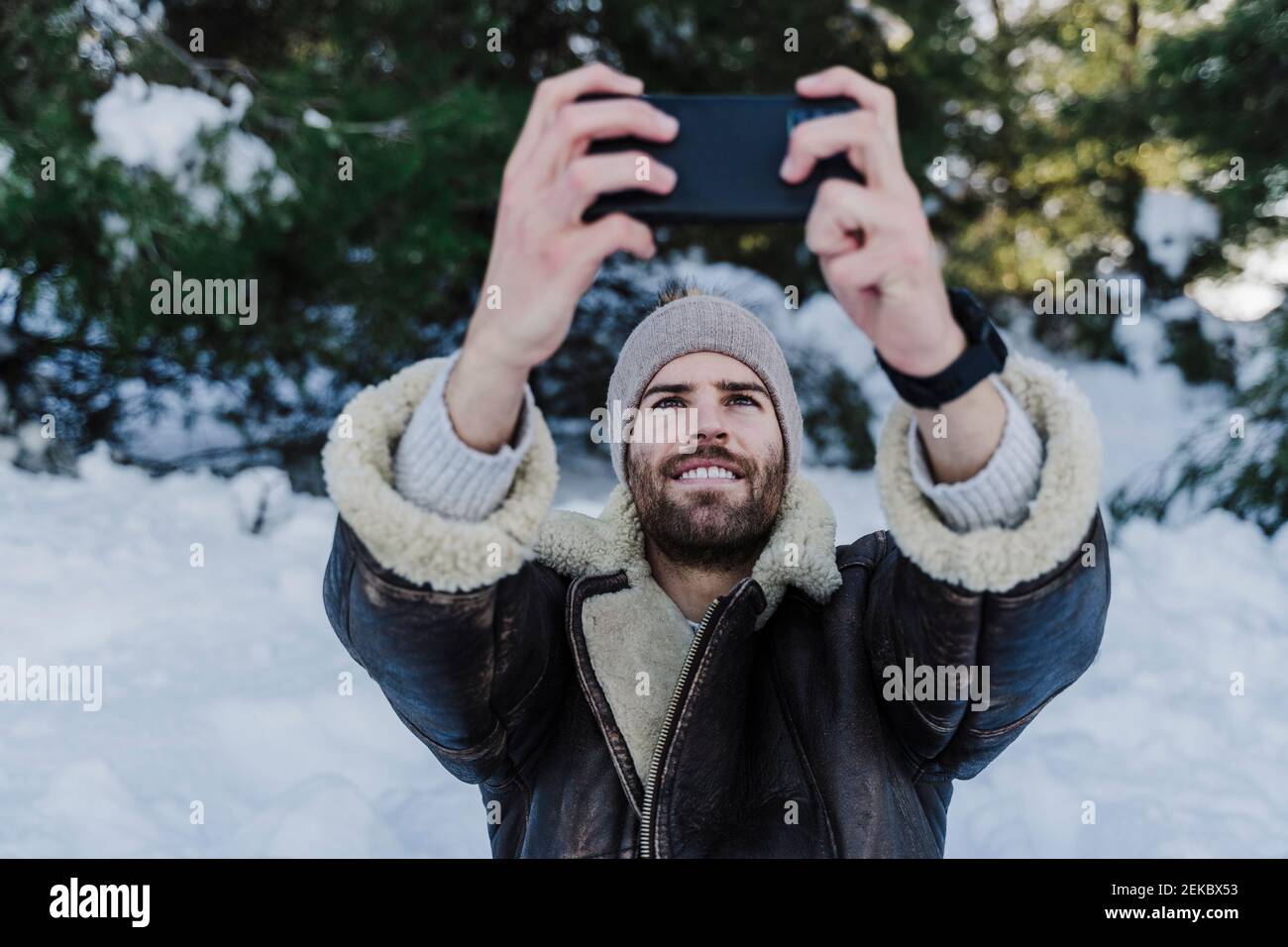 Smiling man in warm clothing taking selfie through smart phone during winter Stock Photo
