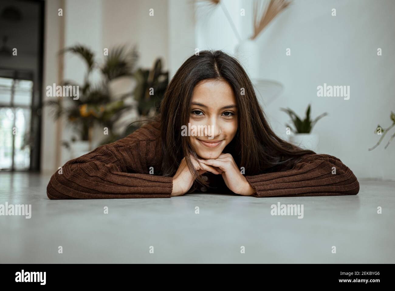 Smiling girl with hand on chin lying on floor at home Stock Photo