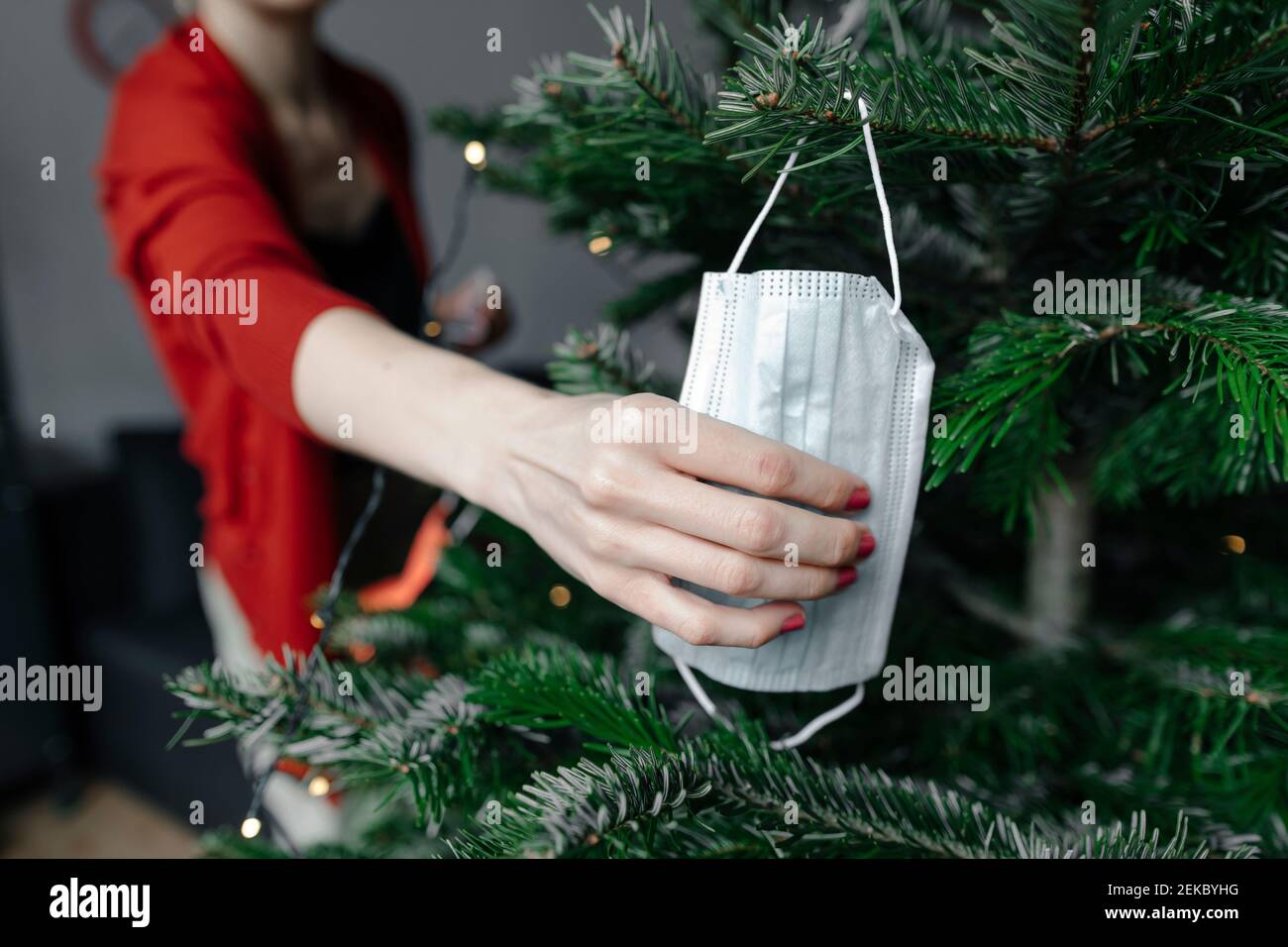 Woman's hand holding protective face mask hanged on Christmas tree at home Stock Photo