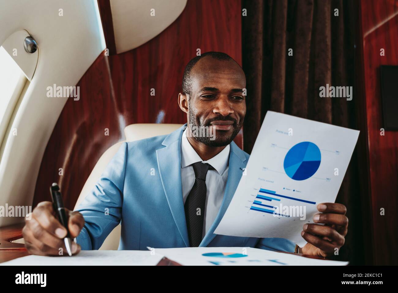 Smiling businessman analyzing graph in private jet Stock Photo
