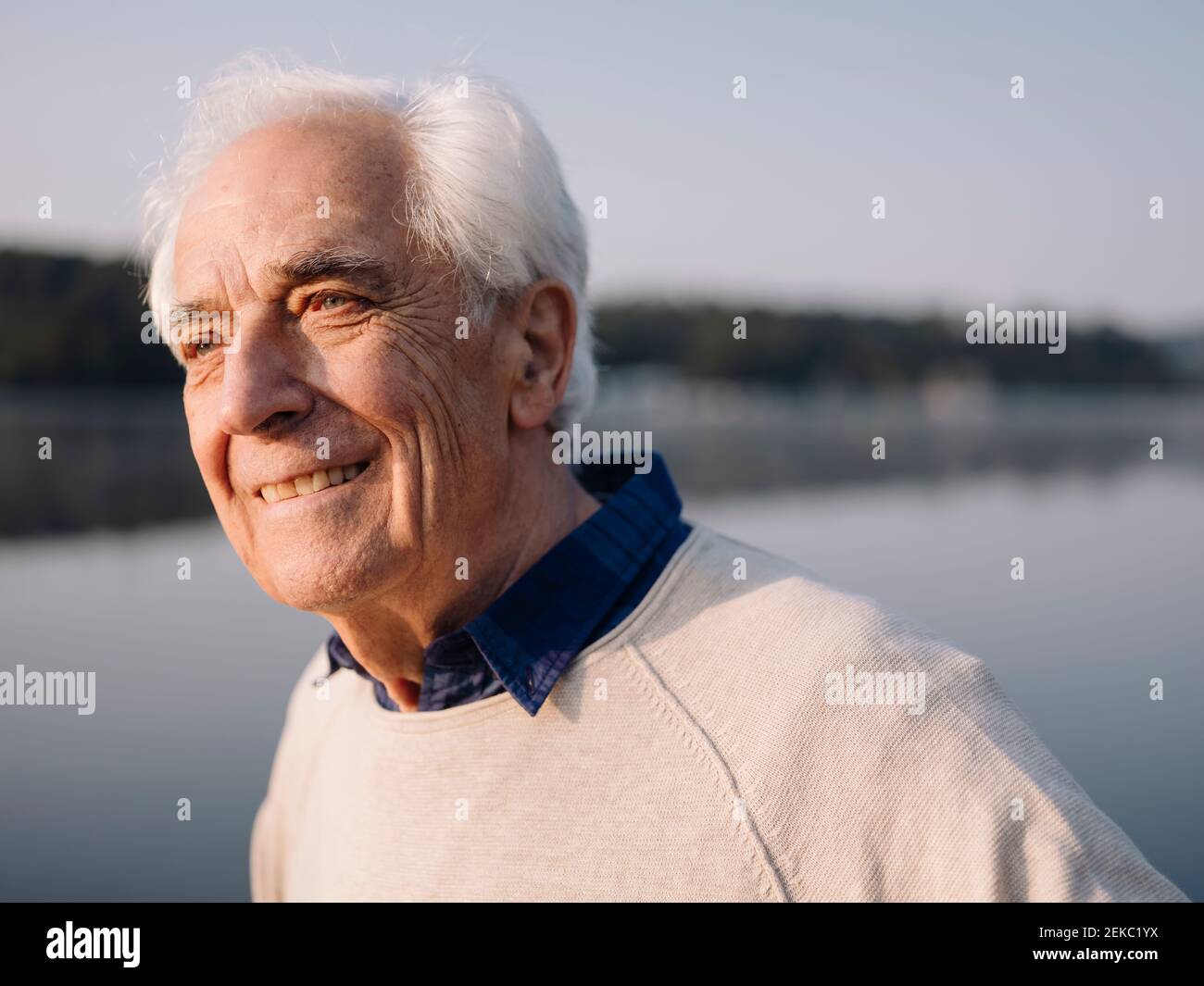 Smiling man looking away while standing against lake Stock Photo