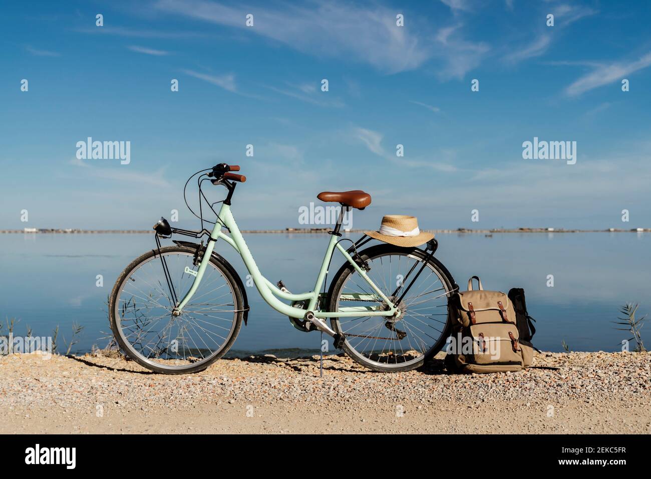 Bicycle parked with backpack leaning on rear wheel with hat on sunny day at Ebro's Delta. Spain Stock Photo