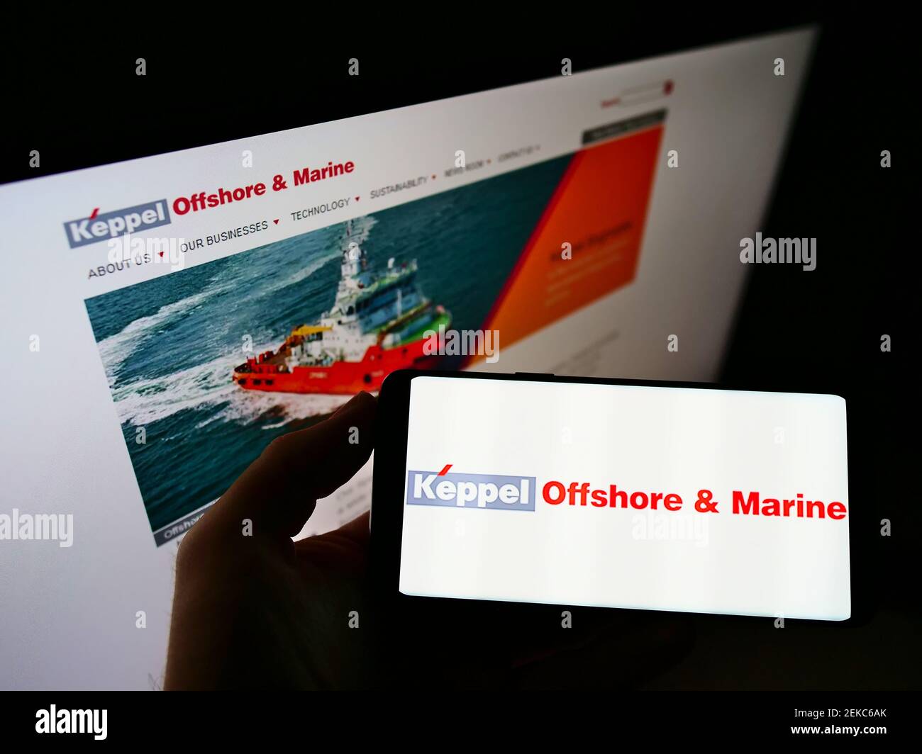 Person holding cellphone with business logo of Singaporean company Keppel Offshore and Marine on screen in front of website. Focus on phone display. Stock Photo