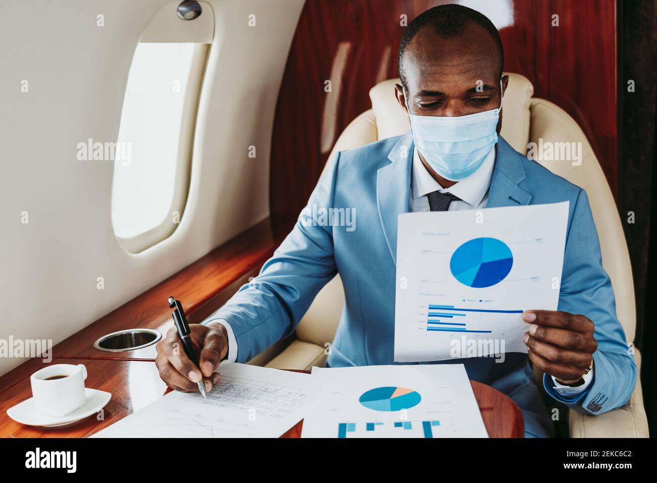 Young businessman analyzing graph while working in airplane during COVID-19 Stock Photo