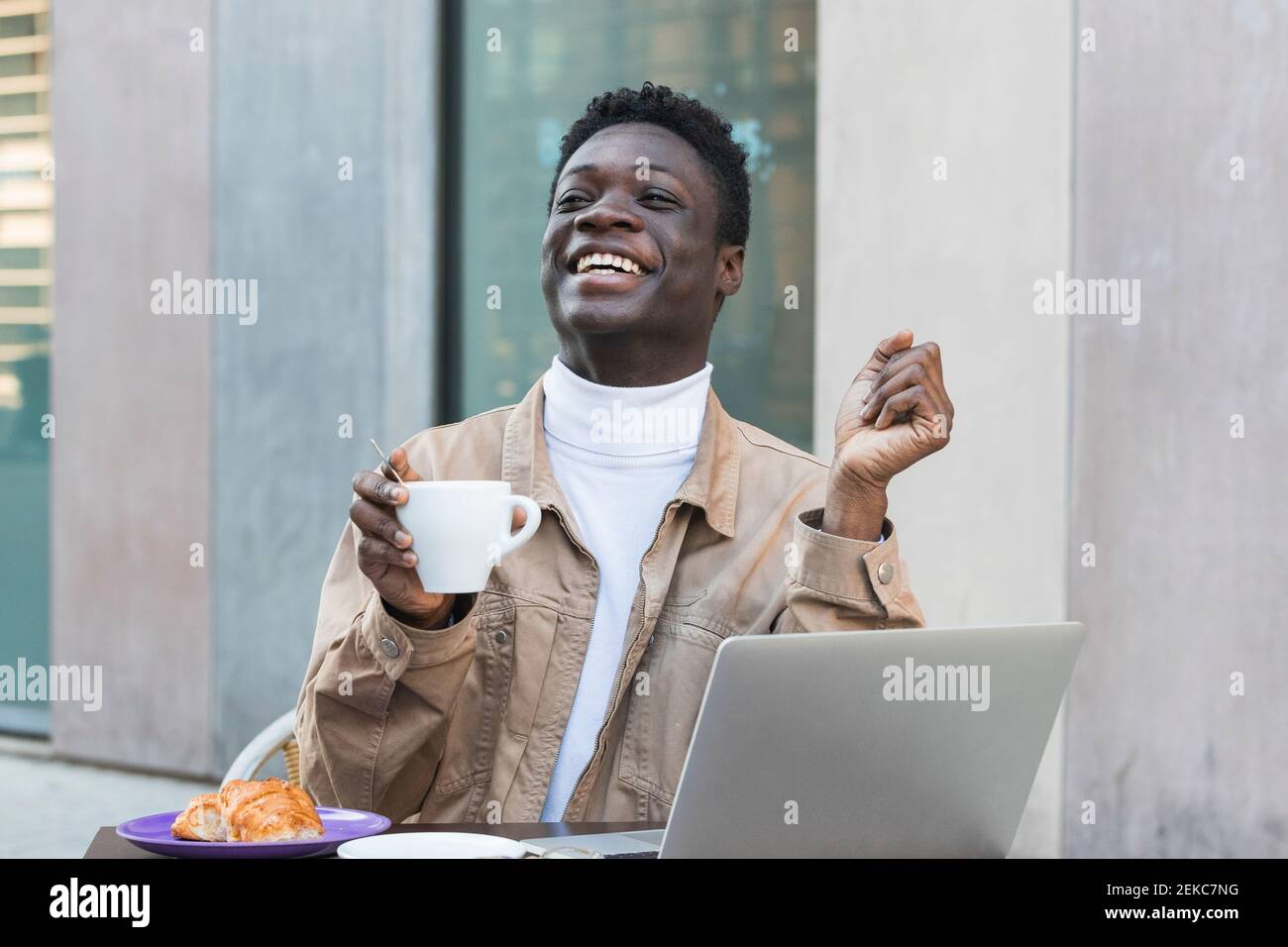 Happy African man with laptop holding coffee cup at sidewalk cafe Stock Photo
