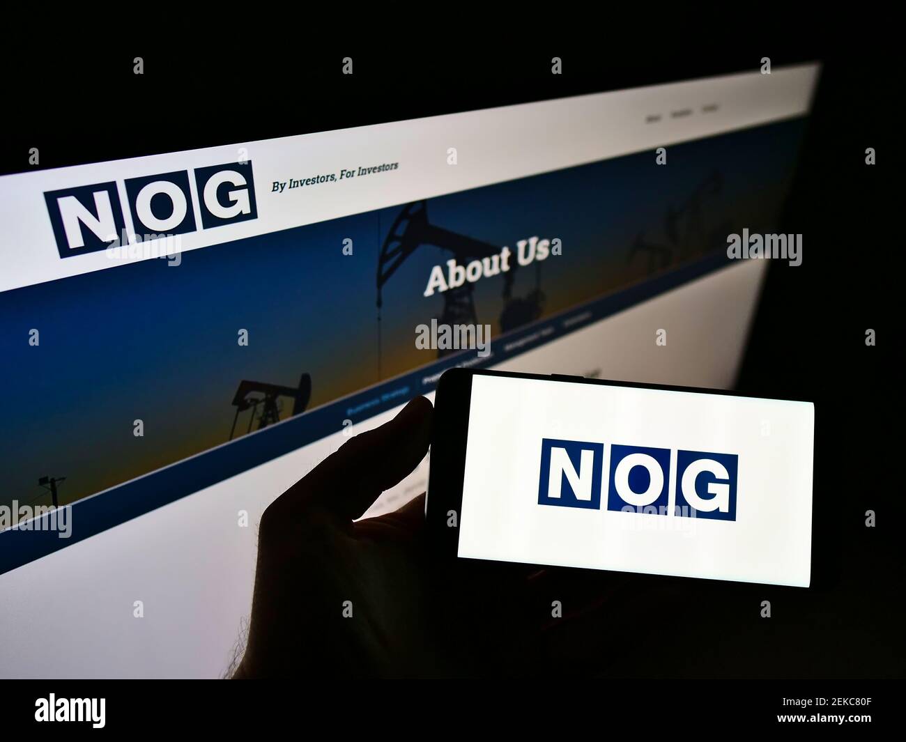 Person holding mobile phone with logo of American oil company Northern Oil and Gas Inc. (NOG) on screen in front of web page. Focus on phone display. Stock Photo