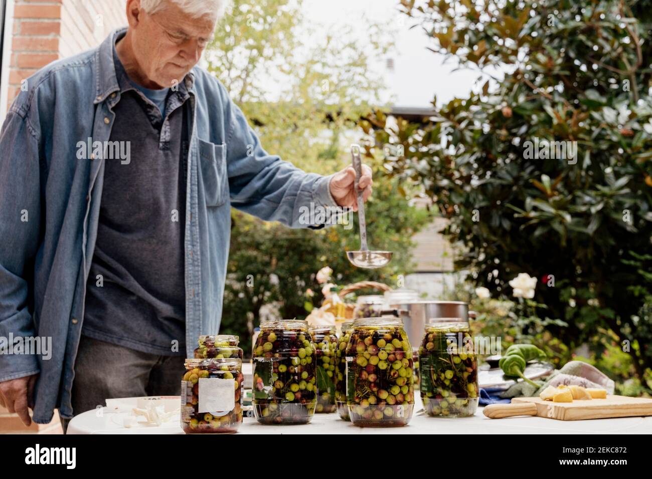 Senior man preparing olives in jars on table at back yard Stock Photo