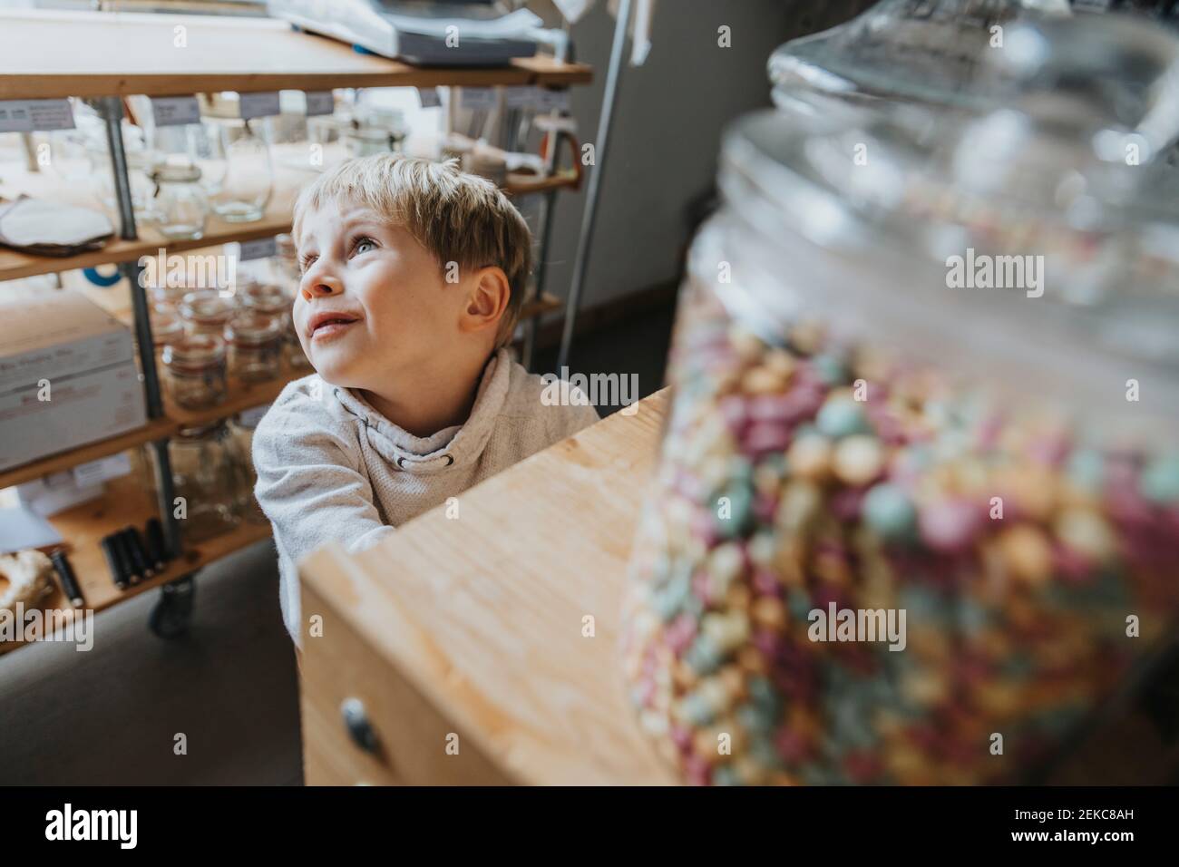Blond little boy day dreaming while standing in candy store Stock Photo