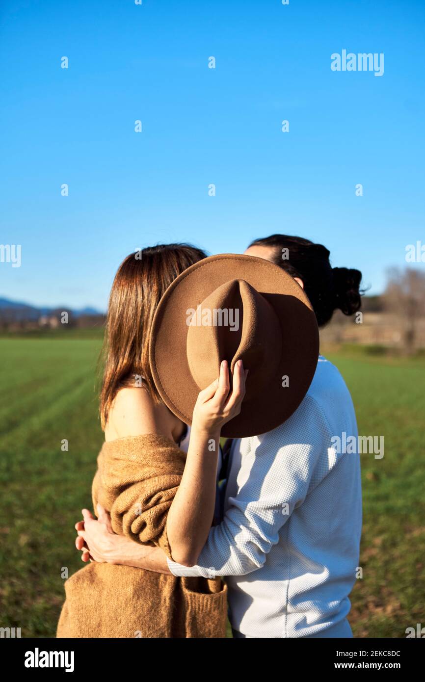 Couple embracing while girlfriend covering faces through hat against blue sky Stock Photo