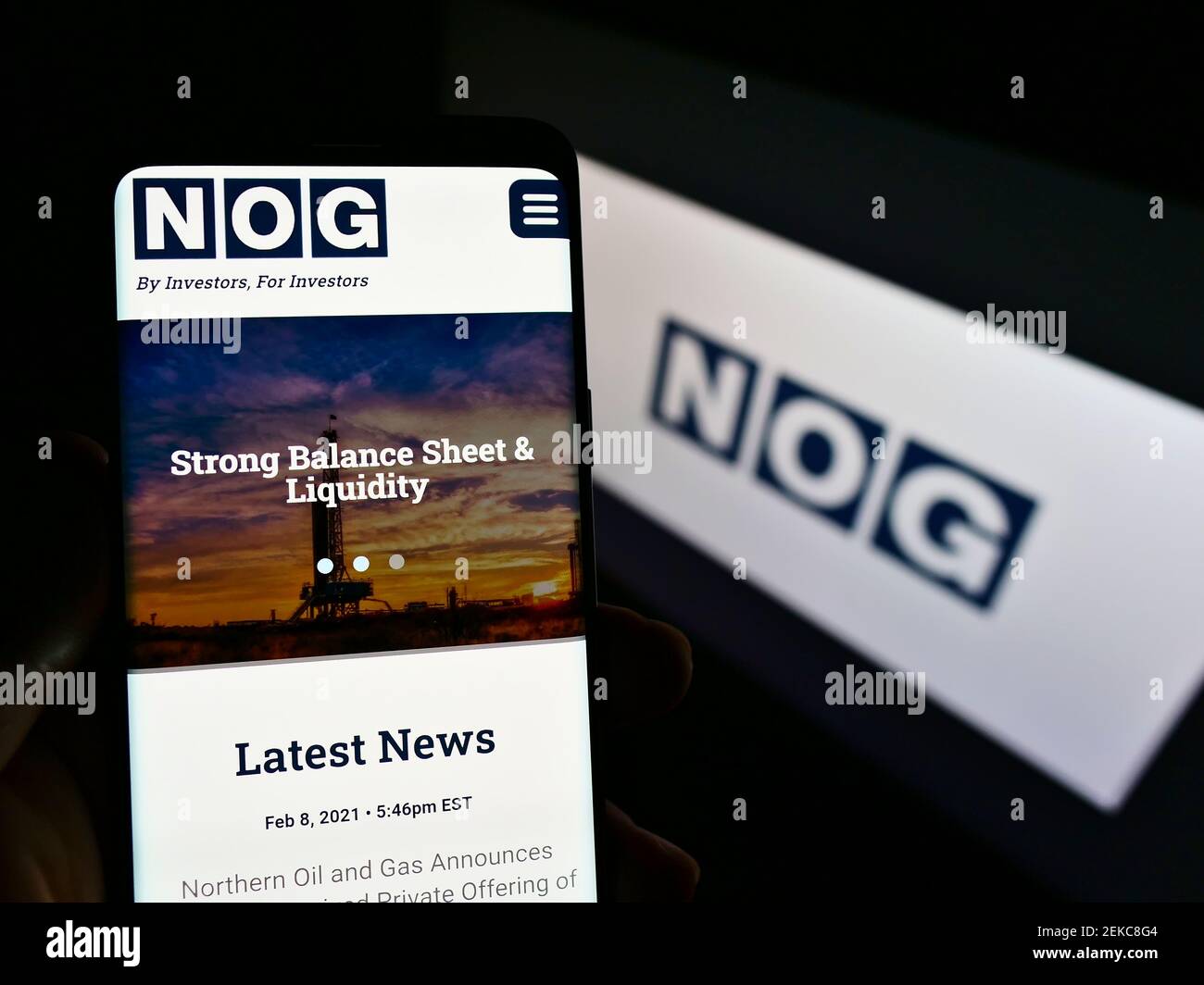 Person holding mobile phone with webpage of US oil company Northern Oil and Gas (NOG) on screen in front of logo. Focus on center of phone display. Stock Photo