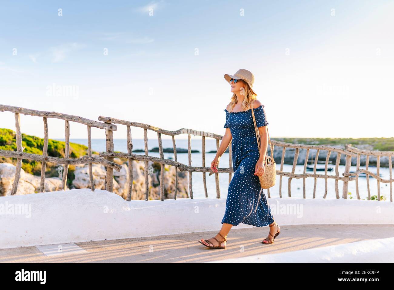 Female tourist wearing hat walking on footpath against sky in Binibeca village, Minorca, Spain Stock Photo