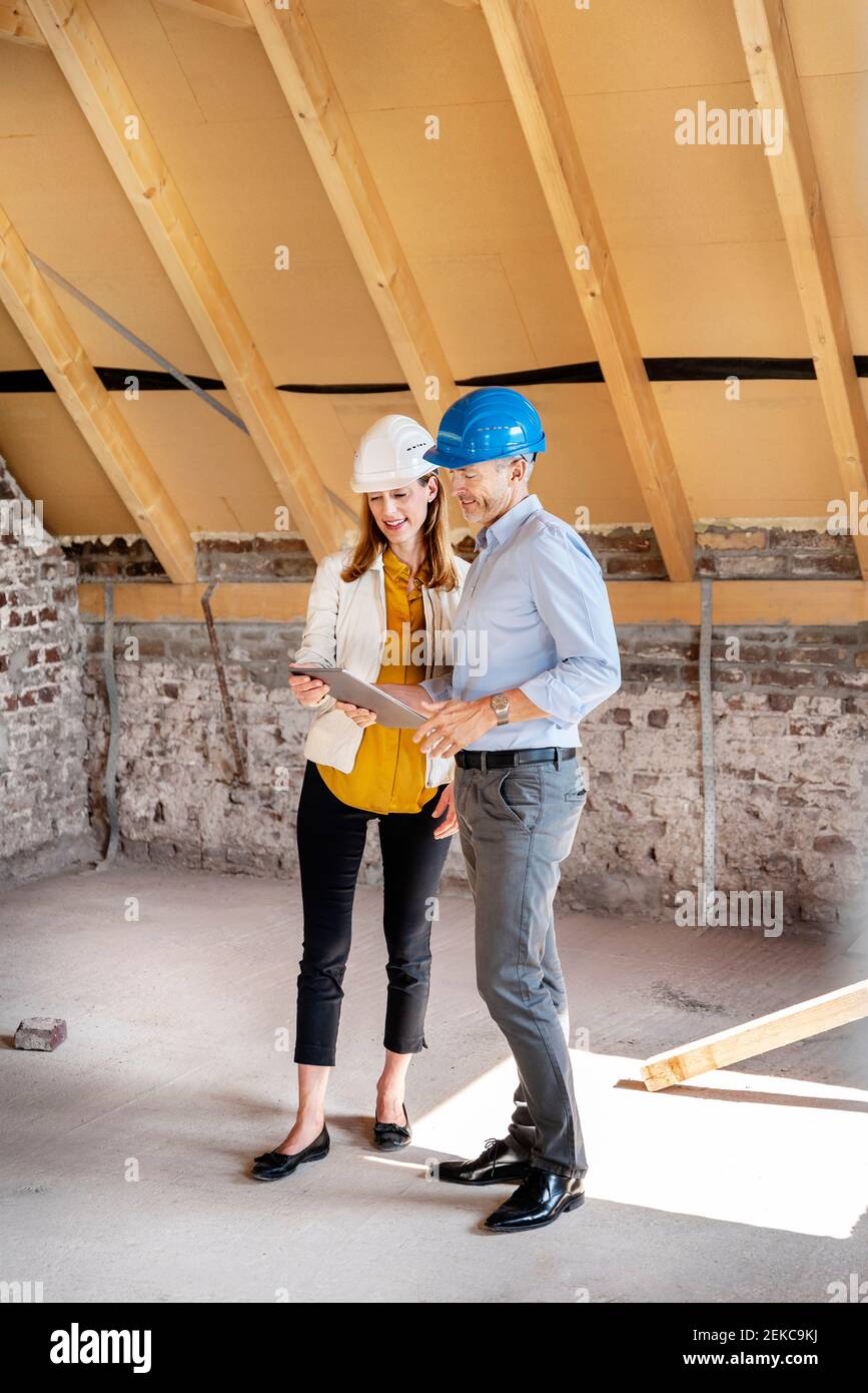 Colleagues wearing hardhat using digital tablet while standing at construction site Stock Photo
